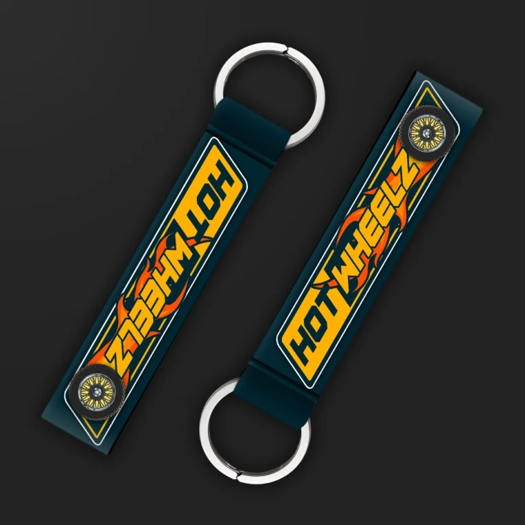 Inline-4 Hot Wheelz keychain strap with orange flame lettering, alloy-wheel icons, and a navy diamond-plate background, double keyring