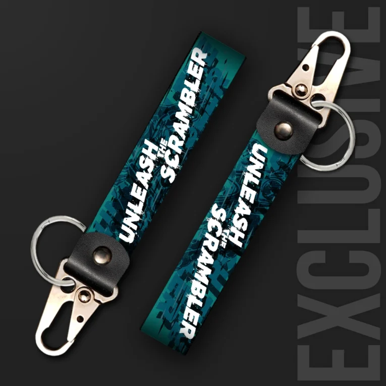 Inline-4 Unleash the Scrambler keychain strap with white 'UNLEASH THE SCRAMBLER' text over a teal off-road motorcycle illustration, swivel hook clip + keyring