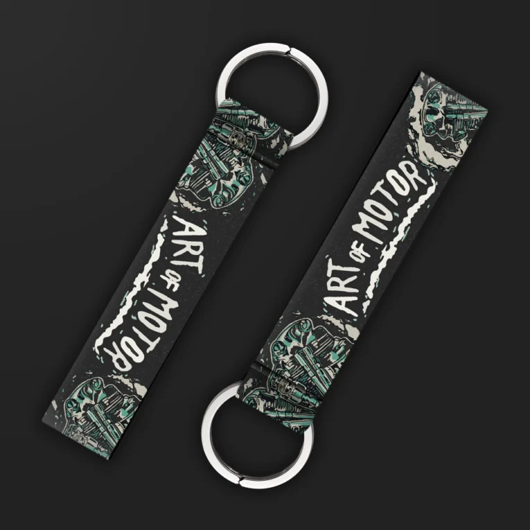 Inline-4 Art of Motor keychain strap with white 'ART OF MOTOR' text over teal engine-piston illustrations on black, double keyring