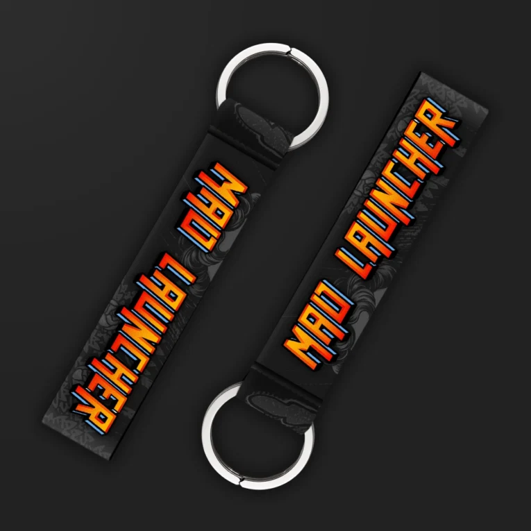 Inline-4 Mad Launcher keychain strap with retro arcade-style orange and red 'MAD LAUNCHER' text on a dark textured background, double keyring