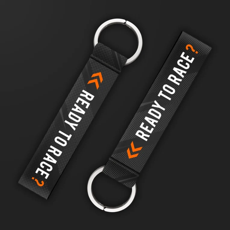 Inline-4 Ready to Race keychain strap with white 'READY TO RACE?' text and an orange chevron icon on a black halftone background, double keyring