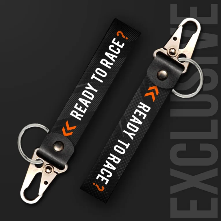 Inline-4 Ready to Race keychain strap with white 'READY TO RACE?' text and an orange chevron icon on a black halftone background, swivel hook clip + keyring