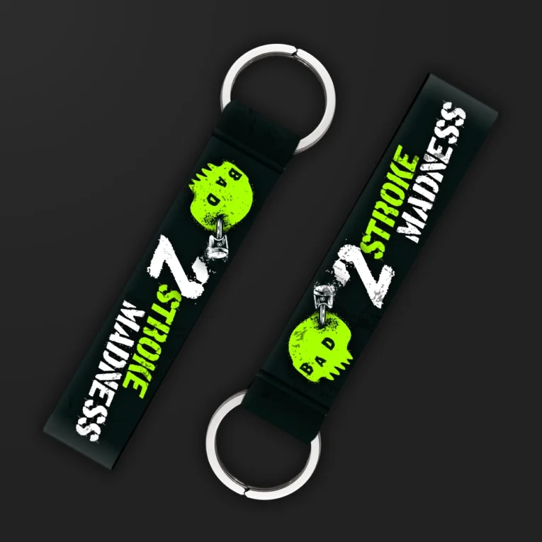 Inline-4 2 Stroke Madness keychain strap with neon-green skull icons, piston graphics, and white '2 STROKE MADNESS' text on black, double keyring