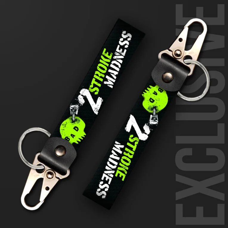 Inline-4 2 Stroke Madness keychain strap with neon-green skull icons, piston graphics, and white '2 STROKE MADNESS' text on black, swivel hook clip + keyring