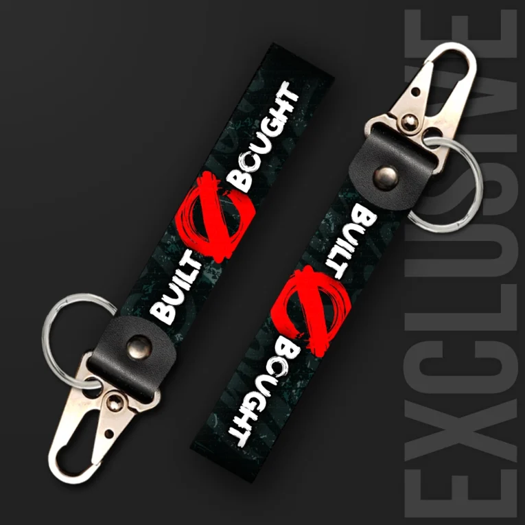 Inline-4 Built Not Bought keychain strap with white 'BUILT' and 'BOUGHT' text crossed out by a red brush stroke on a dark camo background, swivel hook clip + keyring