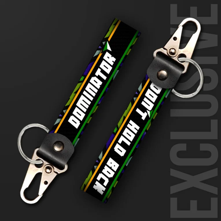 Inline-4 Dominator keychain strap with bold white 'DOMINATOR' and 'DON'T HOLD BACK' text over a retro geometric pattern, swivel hook clip + keyring