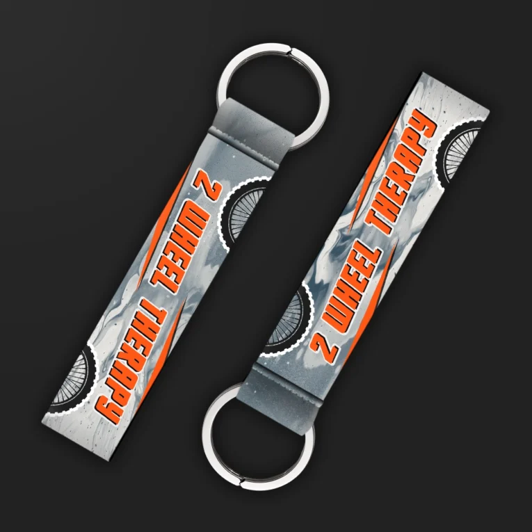 Inline-4 Two Wheel Therapy keychain strap with orange 'TWO WHEEL THERAPY' text over a grey marbled background with wheel icons, double keyring