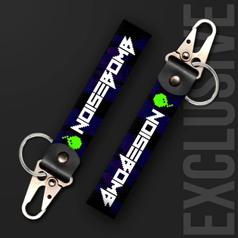 Inline-4 Noisebomb keychain strap with a retro pixel-art skull-bomb icon and 'NOISEBOMB' wordmark on a purple camo print, swivel hook clip + keyring
